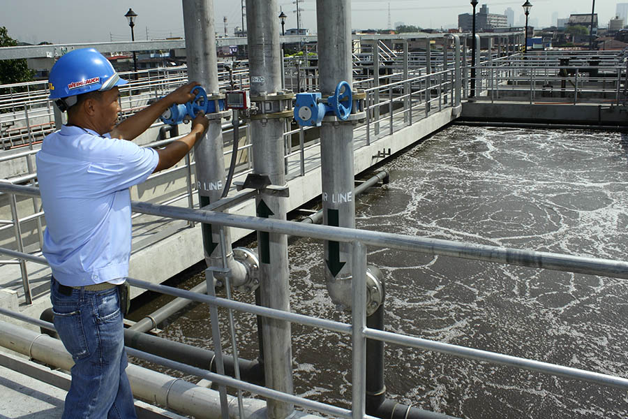 A Worker at a wastewater treatment facility, with pipes and water filtering, with a city in the background. Photo: Danilo Pinzon, World Bank